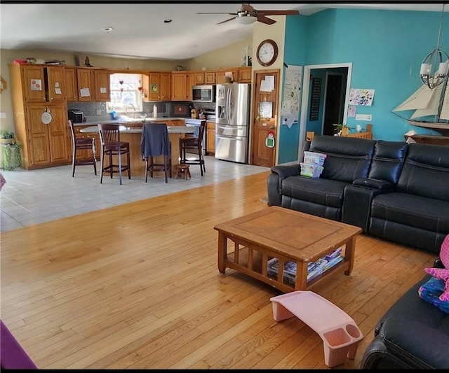 living area with lofted ceiling, ceiling fan with notable chandelier, and light wood-type flooring