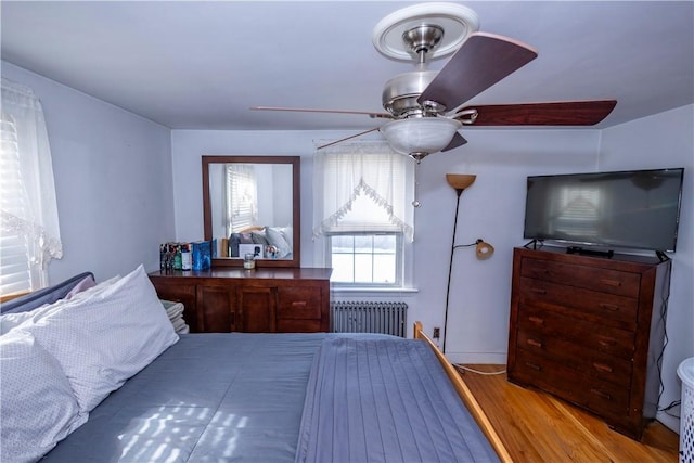 bedroom featuring a ceiling fan, radiator, and wood finished floors