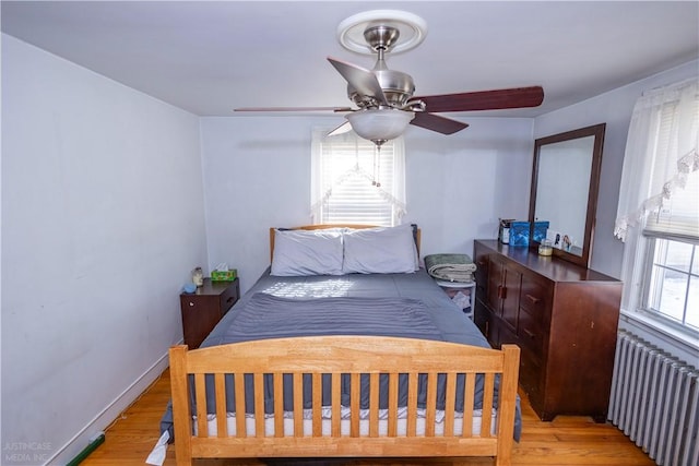 bedroom with baseboards, ceiling fan, light wood-style flooring, and radiator heating unit