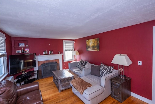 living room featuring light wood-type flooring, a brick fireplace, a textured ceiling, and baseboards