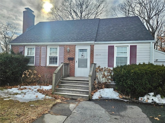 view of front of house featuring roof with shingles, brick siding, and a chimney