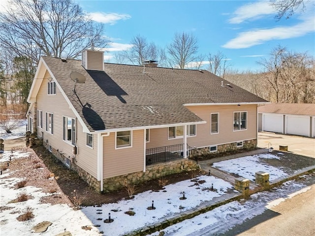 snow covered property with a shingled roof, an outdoor structure, a chimney, and a garage