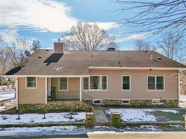 snow covered house featuring covered porch, roof with shingles, and a chimney