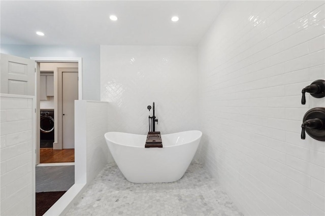 bathroom with washer / clothes dryer, a freestanding bath, and recessed lighting