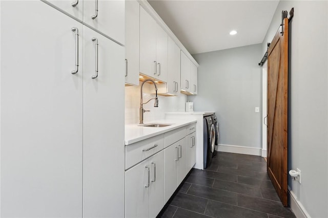 kitchen with a barn door, tasteful backsplash, independent washer and dryer, light countertops, and a sink