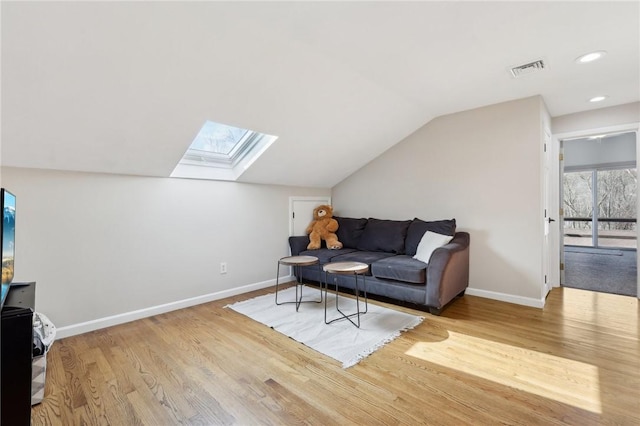 living room featuring lofted ceiling with skylight, baseboards, visible vents, and wood finished floors