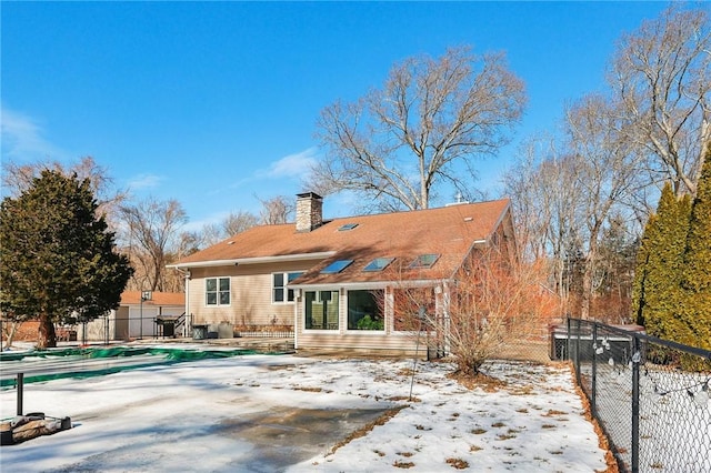 snow covered house featuring a fenced backyard, a chimney, a fenced in pool, and a patio