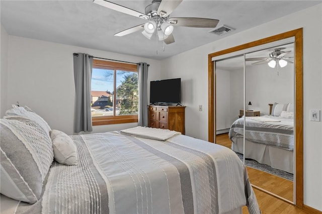 bedroom with a closet, visible vents, a baseboard heating unit, ceiling fan, and wood finished floors