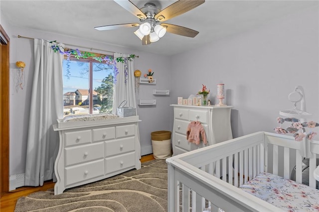 bedroom with a crib, a ceiling fan, and wood finished floors