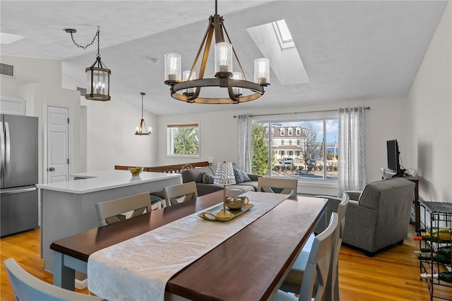 dining room with vaulted ceiling with skylight, visible vents, a notable chandelier, and light wood finished floors