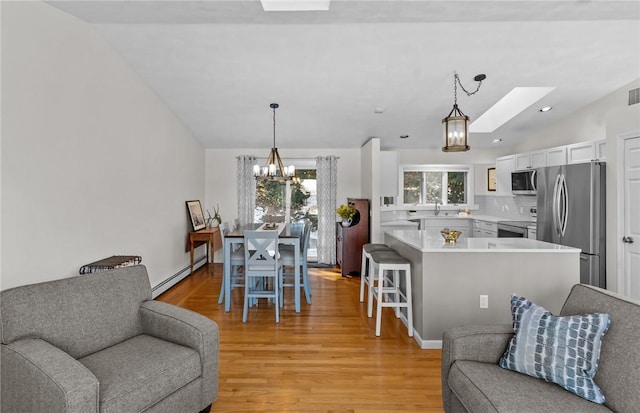 interior space with vaulted ceiling with skylight, light wood finished floors, plenty of natural light, and a baseboard heating unit