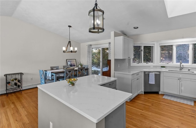 kitchen with light wood finished floors, light stone countertops, vaulted ceiling, stainless steel dishwasher, and a sink