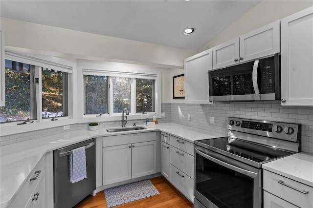 kitchen with light stone counters, light wood-style flooring, stainless steel appliances, a sink, and tasteful backsplash