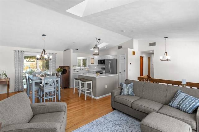 living room featuring a healthy amount of sunlight, light wood-style flooring, visible vents, and a notable chandelier