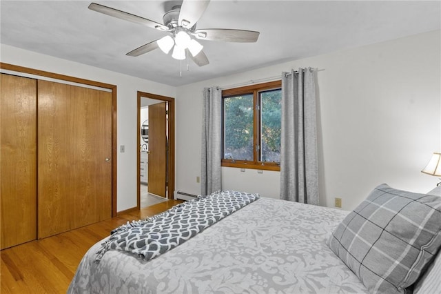 bedroom with a baseboard heating unit, a ceiling fan, a closet, and wood finished floors