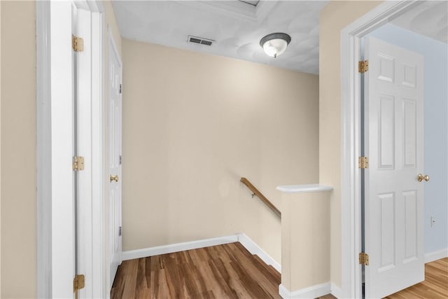 hallway with baseboards, visible vents, an upstairs landing, and wood finished floors