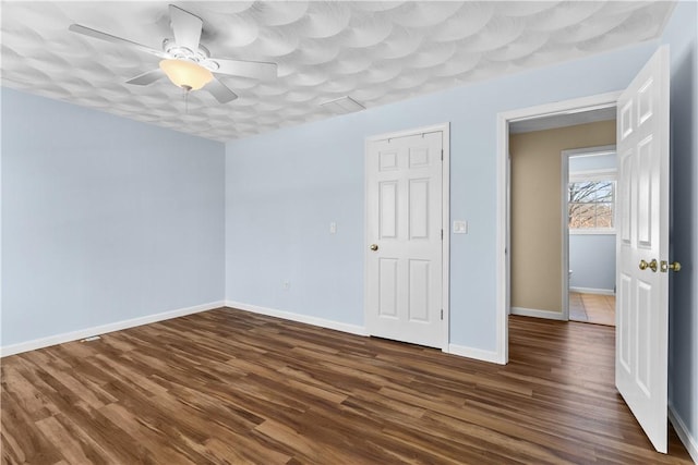 spare room with ceiling fan, visible vents, baseboards, and dark wood finished floors