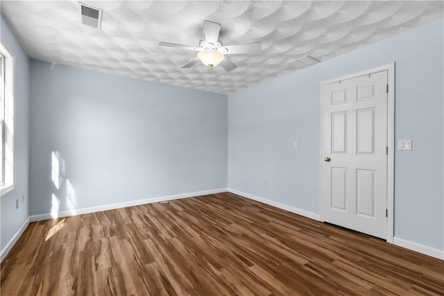 unfurnished room with dark wood-style floors, a ceiling fan, visible vents, and baseboards