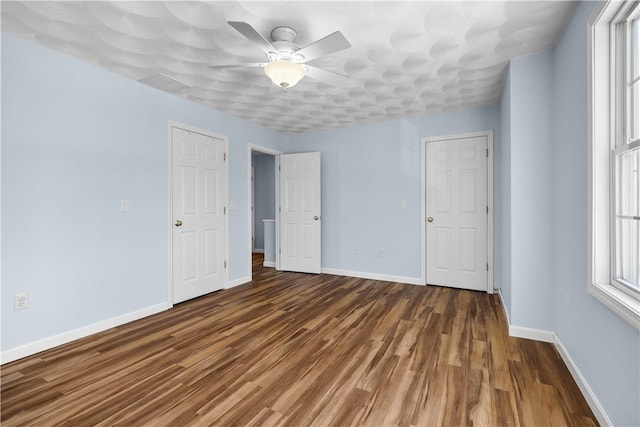 empty room with dark wood-style floors, ceiling fan, and baseboards