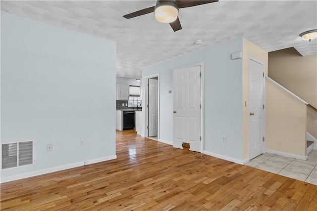 unfurnished living room with stairs, light wood-type flooring, visible vents, and a ceiling fan