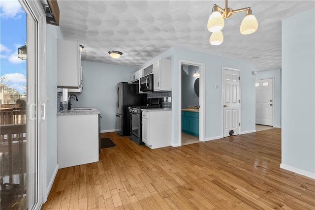 kitchen with black gas range, light wood-style flooring, a sink, white cabinetry, and hanging light fixtures