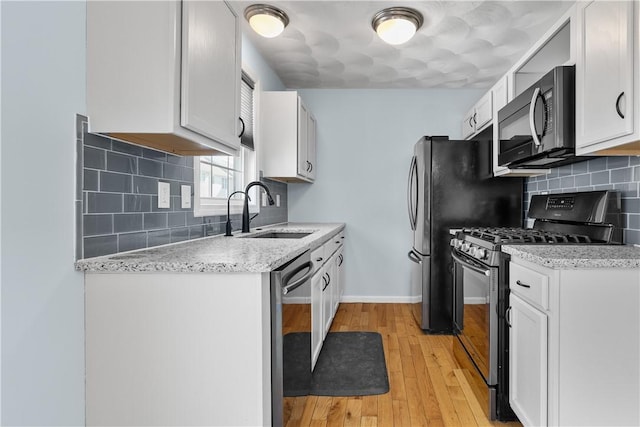 kitchen featuring light wood finished floors, baseboards, appliances with stainless steel finishes, white cabinetry, and a sink