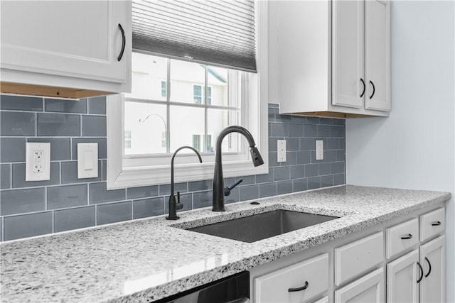 kitchen featuring light stone countertops, white cabinets, and a sink