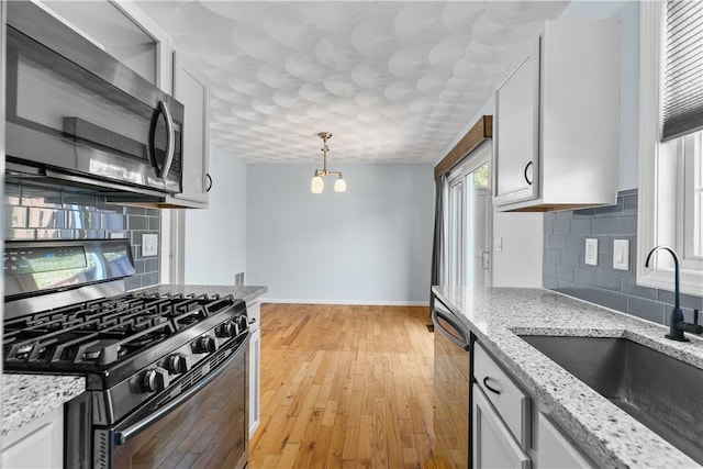 kitchen with white cabinets, appliances with stainless steel finishes, decorative light fixtures, light stone countertops, and a sink