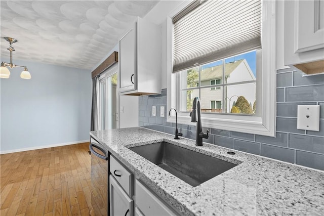 kitchen with decorative backsplash, dishwasher, decorative light fixtures, light stone countertops, and a sink