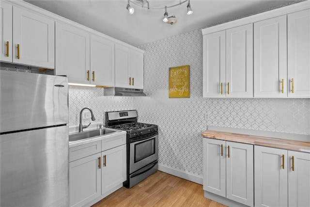 kitchen featuring under cabinet range hood, stainless steel appliances, a sink, wood counters, and wallpapered walls