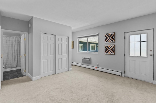 unfurnished bedroom featuring carpet, a baseboard radiator, a closet, ensuite bath, and a wall mounted air conditioner