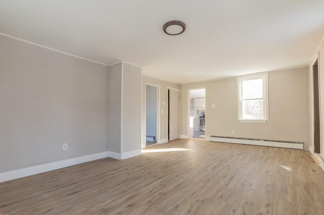 spare room featuring a baseboard heating unit, light wood-style floors, baseboards, and ornamental molding