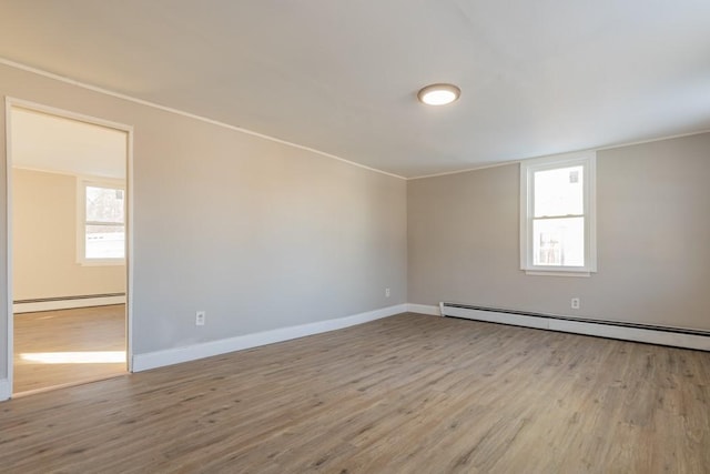 spare room featuring a baseboard radiator, baseboards, light wood-style flooring, and crown molding