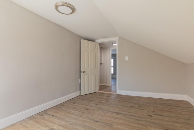 additional living space featuring light wood finished floors, baseboards, and vaulted ceiling