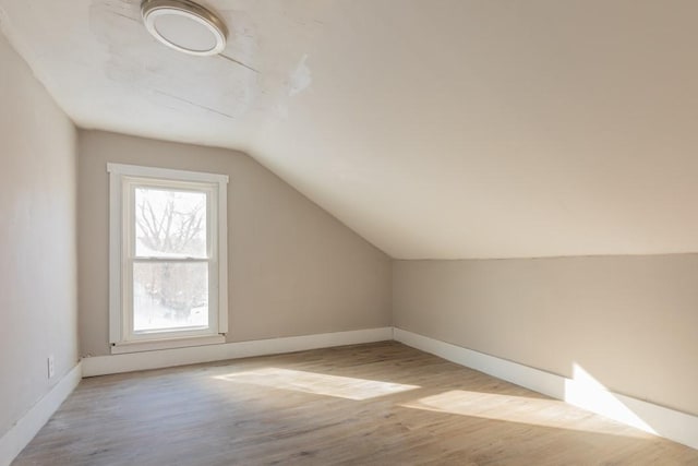 additional living space with light wood-style flooring, baseboards, and vaulted ceiling