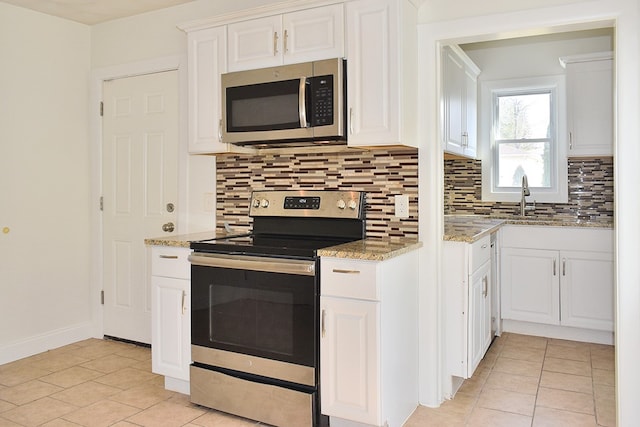 kitchen featuring decorative backsplash, light stone counters, stainless steel appliances, white cabinetry, and a sink