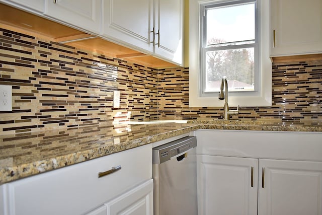 kitchen featuring tasteful backsplash, stainless steel dishwasher, light stone countertops, and white cabinets