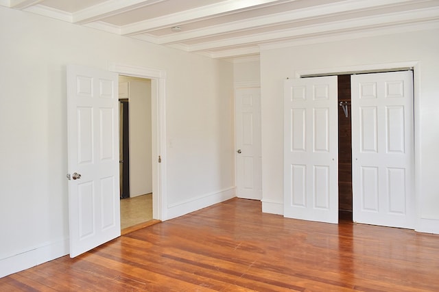 unfurnished bedroom with a closet, wood finished floors, beam ceiling, and baseboards