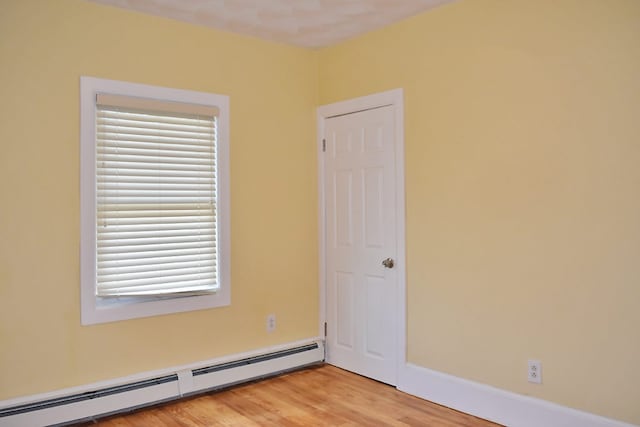 spare room with a baseboard heating unit, light wood-style flooring, and baseboards