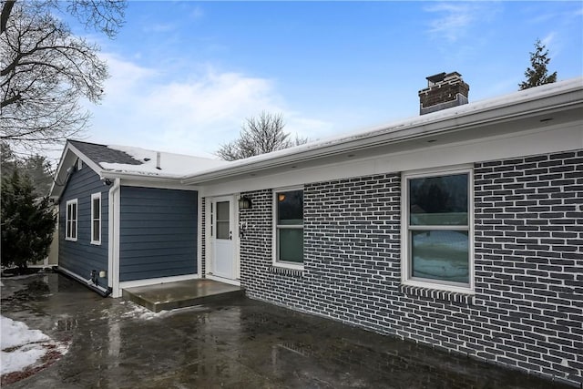 view of front of home featuring a patio, brick siding, and a chimney