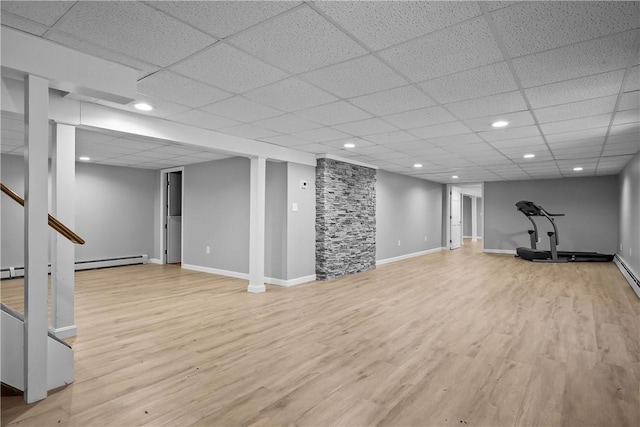 finished basement with a baseboard heating unit, a drop ceiling, light wood-style flooring, and baseboards