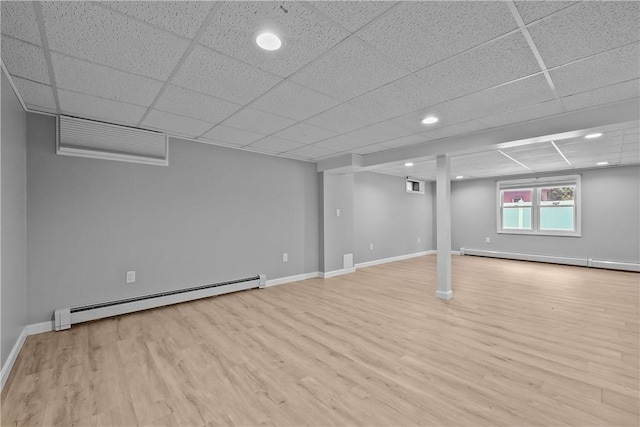 below grade area featuring light wood-type flooring, a baseboard radiator, a baseboard heating unit, and a drop ceiling