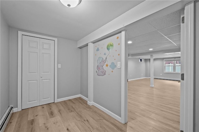 interior space featuring a baseboard heating unit, light wood-type flooring, and baseboards