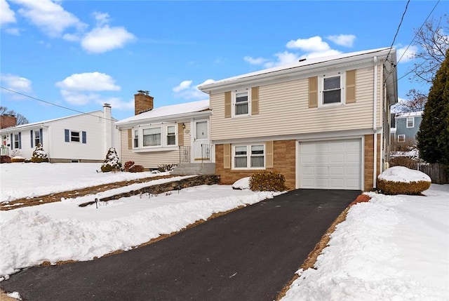 split level home with driveway, a chimney, and an attached garage