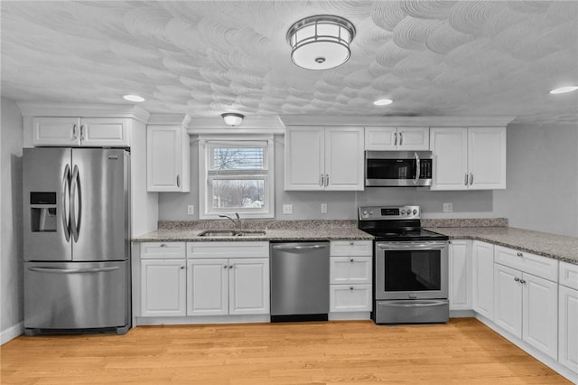 kitchen with stainless steel appliances, light stone counters, a sink, and white cabinets