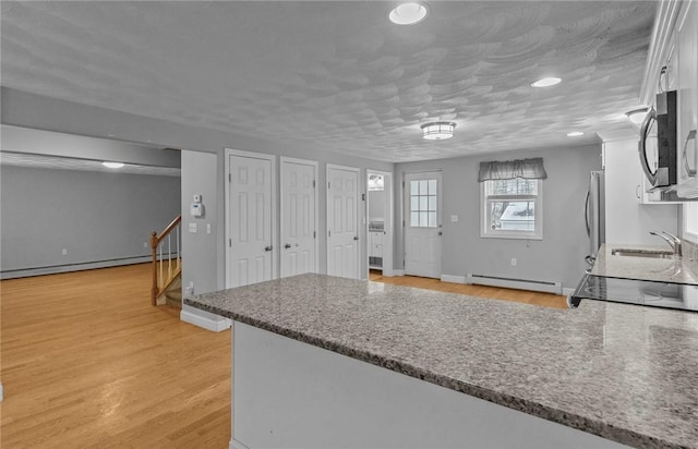 kitchen featuring white cabinets, light wood-style flooring, appliances with stainless steel finishes, baseboard heating, and a sink