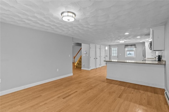 kitchen featuring stone counters, light wood-style flooring, baseboard heating, white cabinets, and baseboards