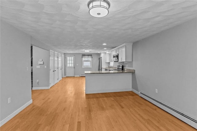 kitchen featuring stainless steel appliances, dark countertops, a baseboard heating unit, white cabinets, and light wood-type flooring