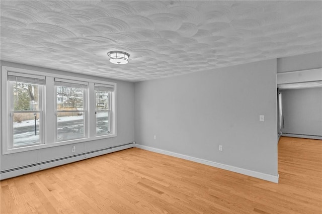 empty room featuring a textured ceiling, a baseboard radiator, light wood-style flooring, and baseboards