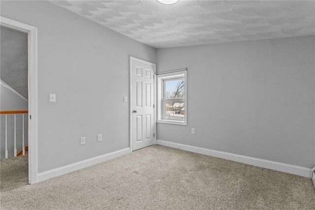 unfurnished room with a textured ceiling, carpet floors, and baseboards